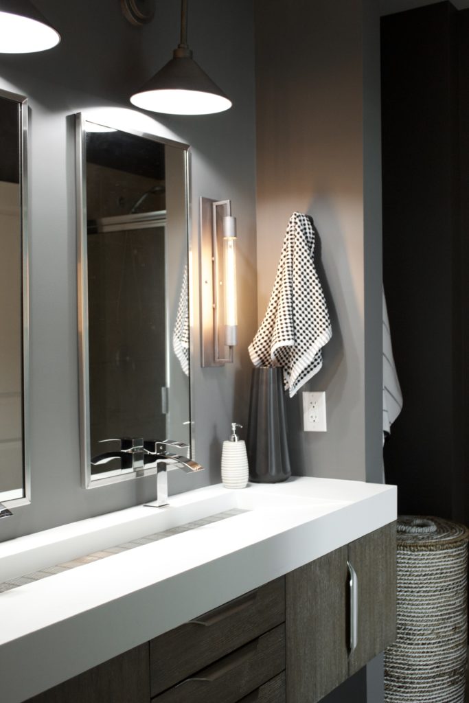 Our Encore Condo project features a modern masculine owner's bathroom with a wall-mounted double floating vanity and 4" thick integrated matte white trough sink against dark gray walls. #modernmasculine #ownersbathroom #condobathrooms #BehrAsphaltGray