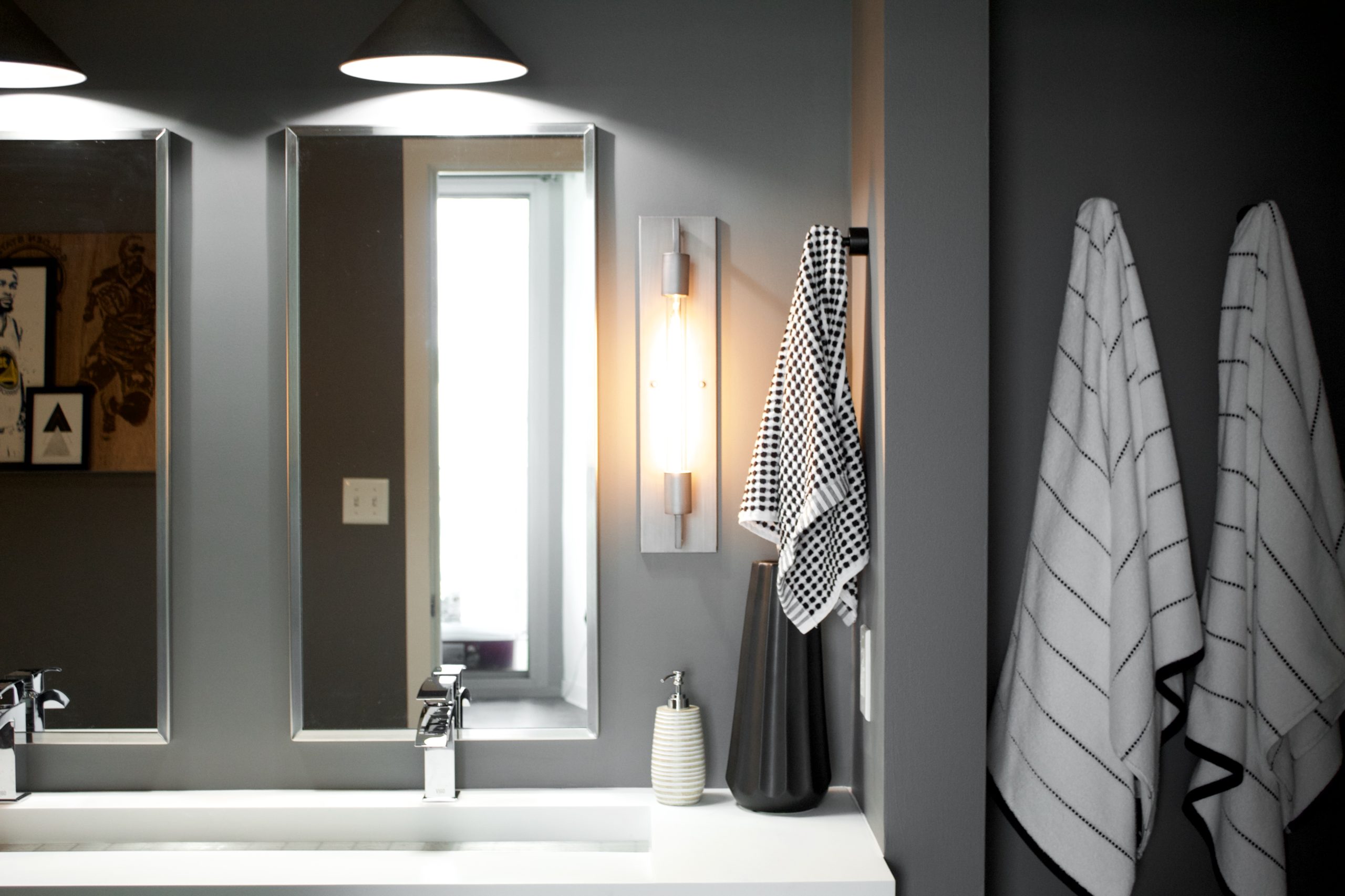 Our Encore Condo project features a modern masculine owner's bathroom with a wall-mounted double floating vanity and 4" thick integrated matte white trough sink against dark gray walls. #modernmasculine #ownersbathroom #condobathrooms #BehrAsphaltGray