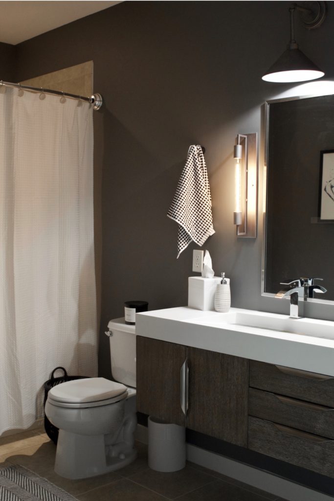 Our Encore Condo project features a modern masculine owner's bathroom with a wall-mounted double floating vanity and 4" thick integrated matte white trough sink against dark gray walls. #modernmasculine #ownersbathroom #condobathrooms #BehrAsphaltGray