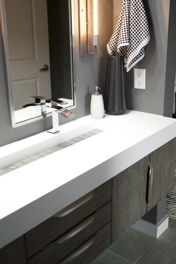 Our Encore Condo project features a modern masculine owner's bathroom with a wall-mounted double floating vanity and 4" thick integrated matte white trough sink against dark gray walls. #modernmasculine #ownersbathroom #condobathrooms #BehrAsphaltGray