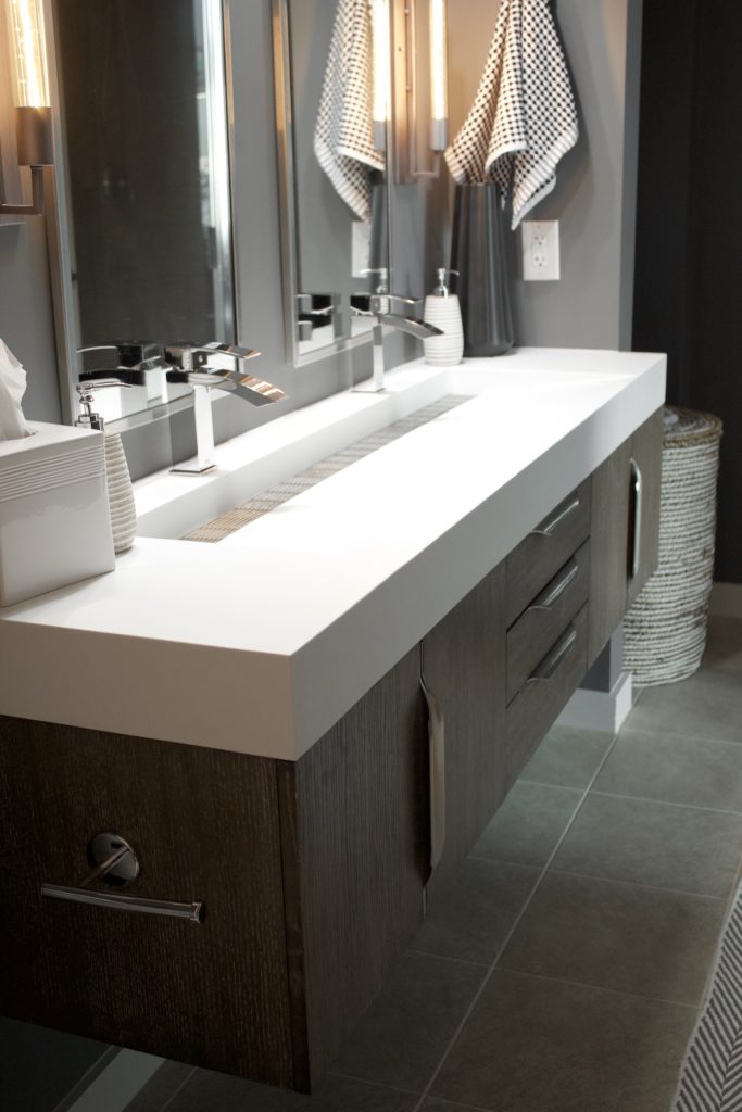 Our Encore Condo project features a modern masculine owner's bathroom with a wall-mounted double floating vanity and 4" thick integrated matte white trough sink against dark gray walls. #modernmasculine #ownersbathroom #condobathrooms #BehrAsphaltGray