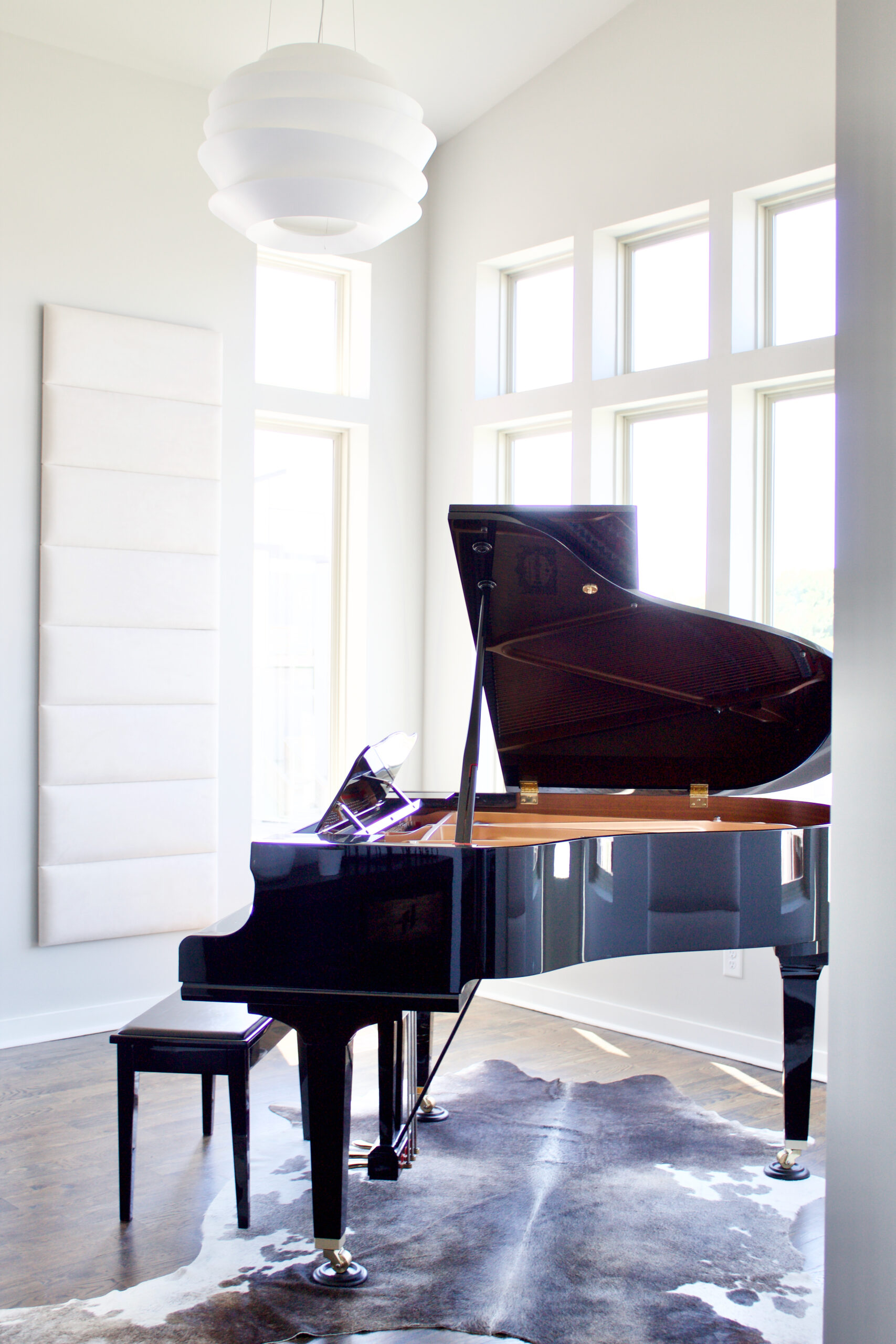 The foyer of our #MinimalModernSouthNashville project features modern entry lighting suspended over a baby grand piano with large windows on three walls and a sloped ceiling that reaches 15'H. The spherical pendant is made of white bands that diffuse the light and create a soft, dimensional glow. Light is also projected directly upward and downward to dramatically highlight the space, making it the perfect welcoming statement piece. Interior wall and ceiling color is Sherwin Williams Repose Gray SW 7015. The trim is bright white. #SherwinWilliamsReposeGrayInteriorWalls #ReposeGraySW7015 #interiorpaintcolor #lightgrayinteriorpaintcolors
